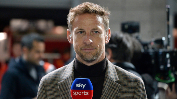 Button in high-neck dark top and beige blazer in the F1 paddock holding a Sky Sports microphone